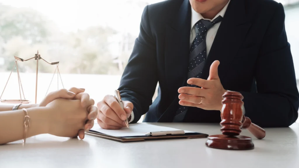 Client meeting with car insurance attorney at office, with gavel and justice scales on desk.