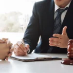 Client meeting with car insurance attorney at office, with gavel and justice scales on desk.