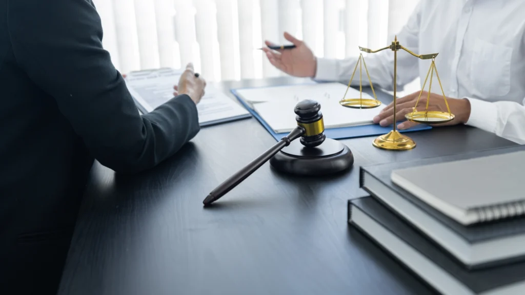 Car insurance claim lawyer reviewing documents with client, gavel and scales of justice on office desk.