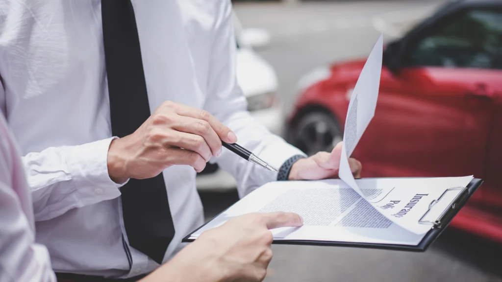 Two people review a Car Insurance Template on a clipboard near a red car after an apparent incident on the road.