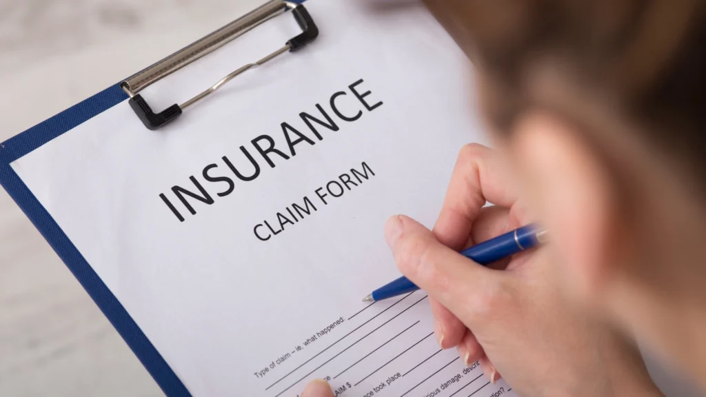 Close-up of car insurance template with a person filling out an insurance claim form using a pen on a clipboard.