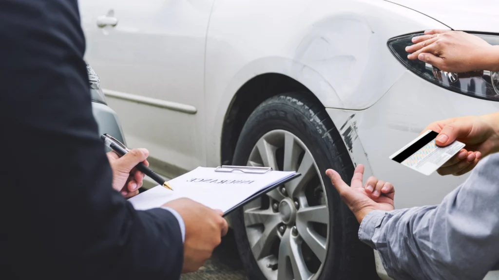 People inspecting a damaged car, discussing paperwork what happens if you don't use insurance money for repairs?