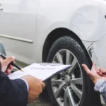 People inspecting a damaged car, discussing paperwork what happens if you don't use insurance money for repairs?