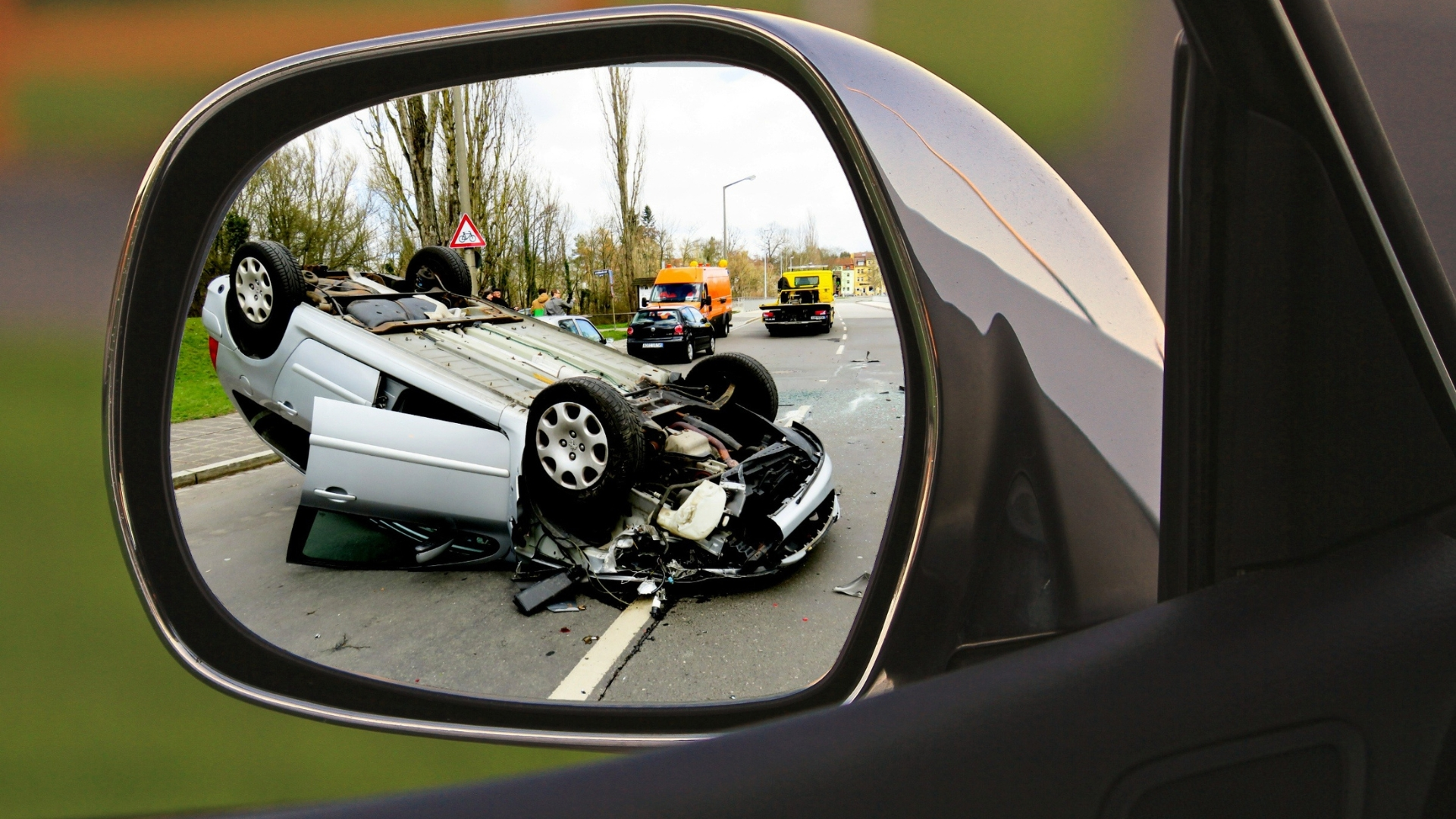Flipped car in mirror highlights real-world need for luxury vs standard accident coverage